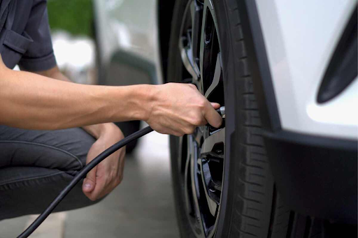 Uma pessoa com a mangueira acoplada no pneu de um carro, calibrando o pneu.